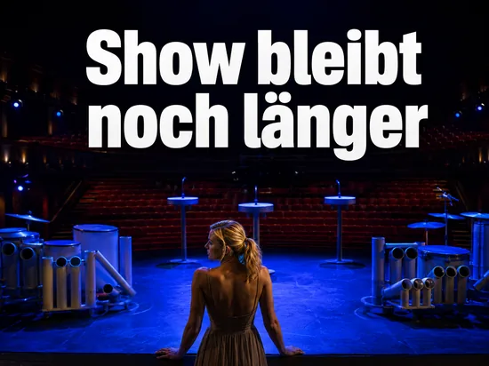 Frau auf einer blau beleuchteten Theaterbuehne mit Rohrtrommeln, Schriftzug Show bleibt noch laenger