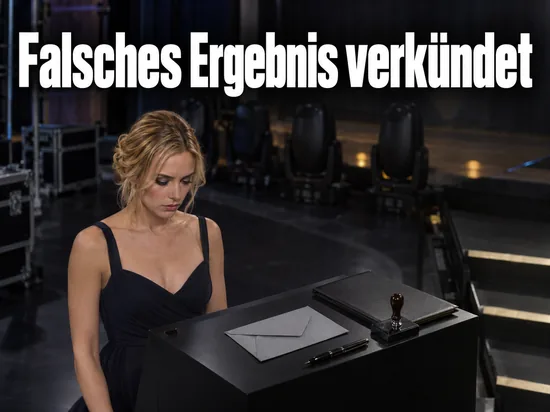 Frau an einem Notarpult mit versiegeltem Umschlag am Rand einer Fernsehbuehne
