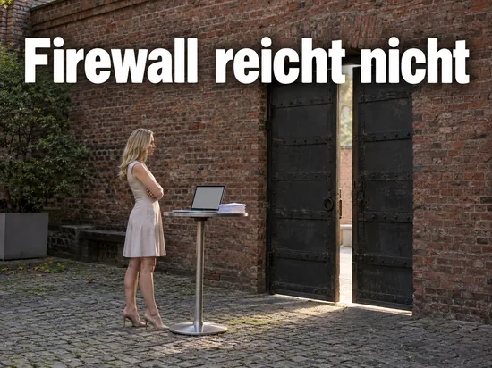 Frau steht in einem Innenhof an einem Stehtisch mit Laptop vor einer Backsteinmauer mit offenem Eisentor