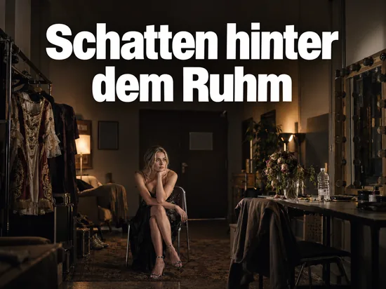 Frau sitzt in einer leeren Theatergarderobe neben einem Schminktisch mit welken Blumen