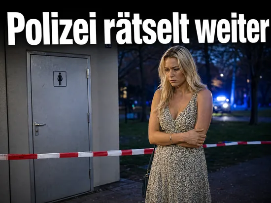 Frau vor abgesperrter Toilettenanlage in einem Park mit Blaulicht im Hintergrund: Polizei raetselt ueber Todesfall