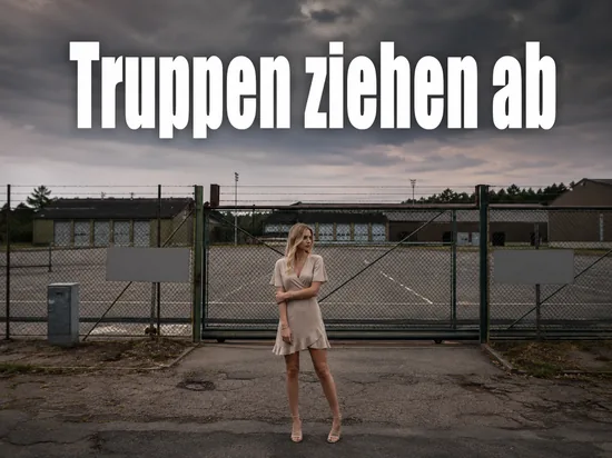 Frau steht vor dem verschlossenen Tor eines verlassenen Kasernengelaendes