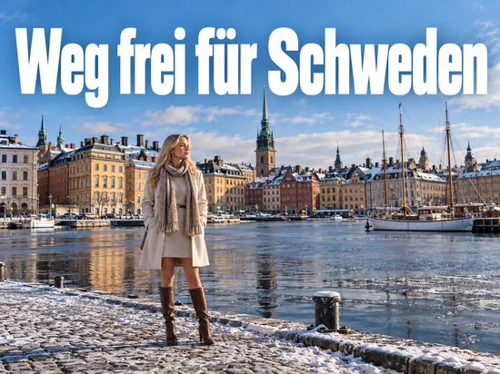 Frau im Wintermantel steht am verschneiten Kai der Stockholmer Altstadt, im Hintergrund bunte Häuser und Segelschiffe