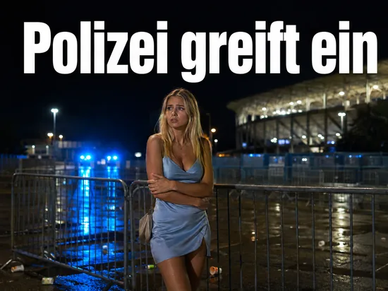 Frau vor Absperrgittern auf einem naechtlichen Stadionvorplatz mit Blaulicht: Polizei beendet Massenschlaegerei
